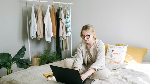 Frau sitz auf dem Bett und betreibt Homeoffice