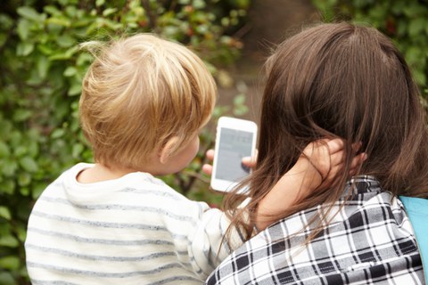 Hinterkopf von Frau und Kind, die beide auf ein Smartphone schauen