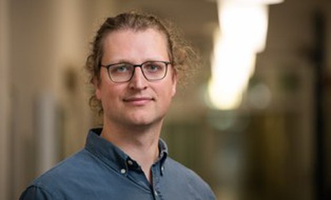 Das Foto zeigt das Portrait eines Mannes, der eine Brille trägt und in die Kamera lächelt.