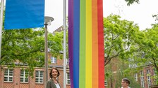 Prorektorin Böhm und Staatssekreträin Dr. Märtens stehen vor der Progressive Pride Flag und halten beide Enden.