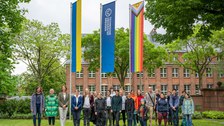 Eine Gruppe von Menschen stehen im Rektoratsgarten vor der Progressive Pride Flag, die TU Dresden Fahne, sowie die Ukrainefahne