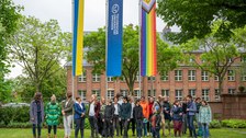 Eine Gruppe von Menschen stehen im Rektoratsgarten vor der Progressive Pride Flag, die TU Dresden Fahne, sowie die Ukrainefahne