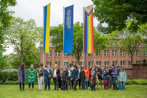 Eine Gruppe von Menschen stehen im Rektoratsgarten vor der Progressive Pride Flag, die TU Dresden Fahne, sowie die Ukrainefahne