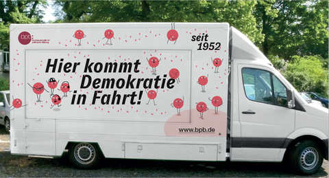 Das Bild zeigt einen Kleinbus mit der Aufschrift "Hier kommt Demokratie in Fahrt".