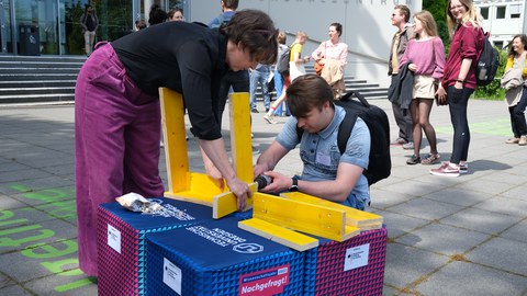 Das Foto zeigt eine Frau und einen Mann, die gemeinsam aus Holzbrettern einen Hocker bauen.