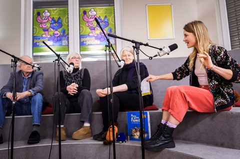 Vier Personen sitzen nebeneinander auf dem Podium. Alle haben ein Mikrofon vor sich und eine Person spricht.