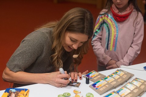 Jana Forkel unterschreibt Autogrammkarten. Neben ihr steht ein kleines Mödchen. 
