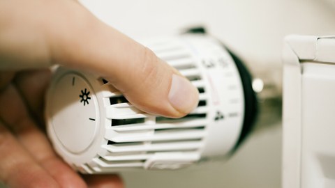 Eine Hand stellt ein Thermostat an einer Heizung ein.