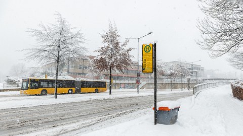 Das Foto zeigt die Bushaltestelle vor dem Hörsaalzentrum der TU Dresden im Winter. Sowohl der Weg zum Gebäude als auch die Straße sind schneebedeckt. 