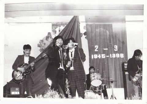 Auf dem Foto sind vier Musiker (2 Sänger, Bass, Gitarre, Schlagzeug) zu sehen. Im Hintergrund hängt ein großes Stofftuch an der Wand, auf dem „2 – 9 1945–1988“ steht.