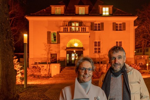 Im Vordergrund des Fotos sind Prof. Dr. Ursula M. Staudinger, Rektorin, und Prof. Dr. Michael Kobel, Prorektor für Bildung zu sehen. Sie stehen vor dem Rektoratsgebäude. Dieses ist orange angestrahlt.