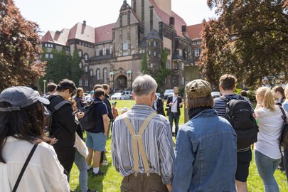 Das Foto zeigt eine Gruppe von Personen, die im Kreis stehen und einem Referenten zuhören.