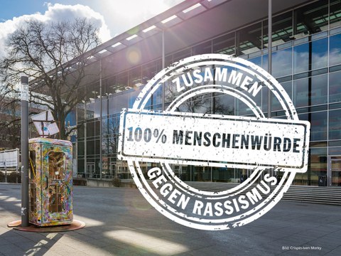 Das Foto zeigt das Hörsaalzentrum von außen (Vorderansicht). Auf das Foto wurde eine Grafik gesetzt. Es ist das Logo der Internationalen Wochen gegen Rassismus.