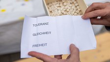 2 Hände halten einen Zettel in die Kamera, auf dem die Worte Toleranz, Gleichheit und Freiheit stehen.