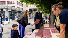 Das Foto zeigt einen kleinen Jungen und Erwachsene, die an Festzelttischen und -bänken stehen. Auf den Bänken und Tischen liegen Karten. Der Junge und eine der Erwachsenen halten jeweils eine Karte in der Hand.