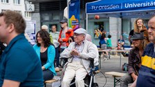 Menschen unterschiedlichen Alters sitzen auf Bänken, die hintereinander stehen.