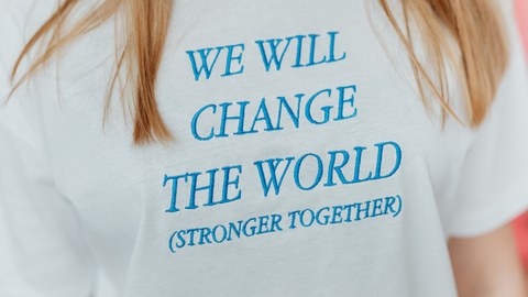 Auf einem T-Shirt ist der Text "We will change the world (stronger together)" ausgestickt.