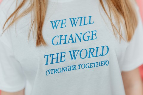 Auf einem T-Shirt ist der Text "We will change the world (stronger together)" ausgestickt.