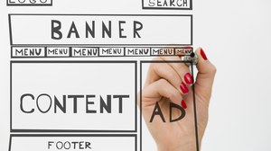 Foto: Abbildung des Aufbaus einer Webseite mit verschieden großen Boxen, welche von einer weiblichen Hand, die hinter der Abbildung zu sehen ist und einen Stift hält, gezeichnet wird.