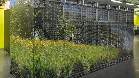 Symbolbild für energieeffizientes Hochleistungsrechnen: Fotomontage aus einem Bild des Supercomputing-Clusters Barnard im Rechnerraum des ZIH und dem Foto einer Blumenwiese und Bäumen, das über das Cluster geblendet wurde. 