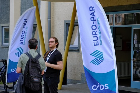 2 Personen im Eingangsbereich zur konferenz - zwischen 2 Beach-Flags mit der Beschriftung Euro-Par 2025 (Logo der Veranstaltung)