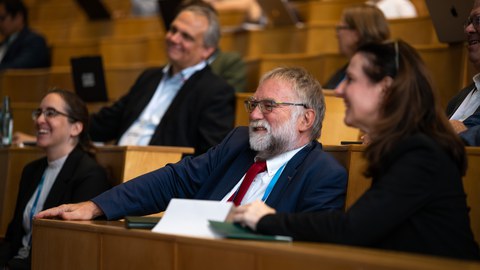 Foto von v.l.n.r.: Prof. Diana Göhringer (TUD), Prof. Martin Schulz (TUM), Prof. Wolfgang E. Nagel (TUD) und Prof. Heike Graßmann (Sächsische Staatssekretärin im SMWKT) als Zuhörende lachend im Auditorium. Im Hintergrund - verschwommen - weitere Zuhörende