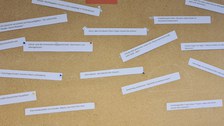 Das Foto zeigt eine Pinnwand weißen rechteckigen beschriebenen Zetteln, die daran gepinnt wurden. In der Mitte der oberen Kante befindet sich ein roter  Zettel, mit dem Text: „original Headlines“.