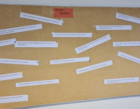 Das Foto zeigt eine Pinnwand weißen rechteckigen beschriebenen Zetteln, die daran gepinnt wurden. In der Mitte der oberen Kante befindet sich ein roter Zettel, mit dem Text: „original Headlines“.