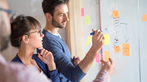 Lehrende schreiben an ein Whiteboard