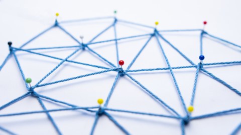 Auf dem Foto sieht man ein Netzwerk aus Stecknadeln und Faden mit vielen Verbindungen.
