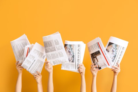 Mehrere Personen halten geöffnete Zeitungen und Magazine vor ihre Gesichter. Sichtbar sind nur ihre Hände und Unterarme. Die Publikationen enthalten Artikel zu Wirtschaft und Finanzen. Der Hintergrund ist einfarbig orange.