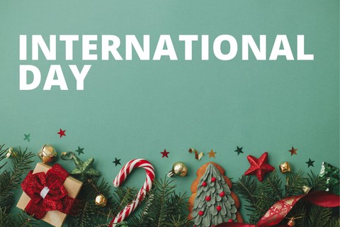 Banner mit der Aufschrift "INTERNATIONAL DAY" und dem Datum "12.12.2024" auf einem grünen Hintergrund. Unten im Bild befinden sich weihnachtliche Dekorationen wie Zuckerstangen, Geschenke, Christbaumschmuck und Tannenzweige.