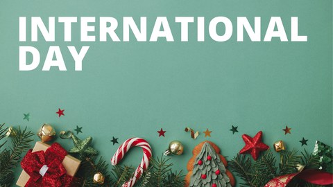 Banner mit der Aufschrift "INTERNATIONAL DAY" und dem Datum "12.12.2024" auf einem grünen Hintergrund. Unten im Bild befinden sich weihnachtliche Dekorationen wie Zuckerstangen, Geschenke, Christbaumschmuck und Tannenzweige.