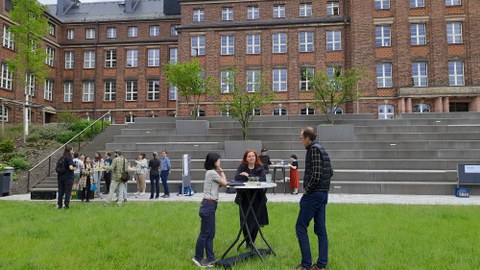 Numerous people are standing on a lawn in front of a large building and chatting.