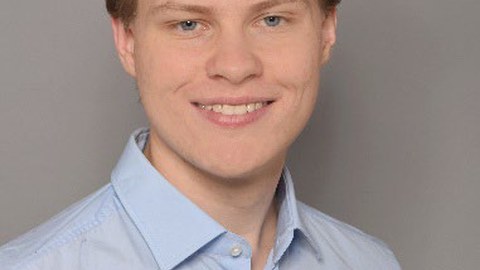 A young man with brown hair is smiling at the camera.
