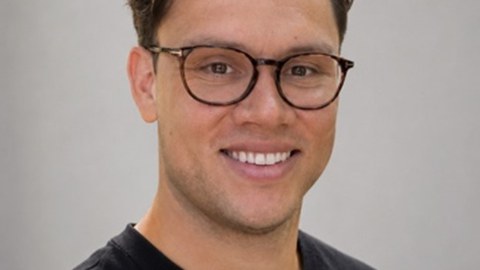 A young man with dark blond hair and glasses smiles at the camera.