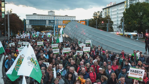 Eine große Menschenmenge bei einer Demonstration in einer deutschen Stadt. Viele Teilnehmer halten Schilder hoch mit Slogans wie „Habeck verhaften“, „Frieden mit Russland“ und „Raus aus der NATO“. Einige tragen sächsische Flaggen. Im Hintergrund sind mode