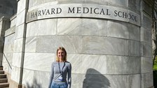 A young woman stands in front of a wall labeled Harvard Medical School.