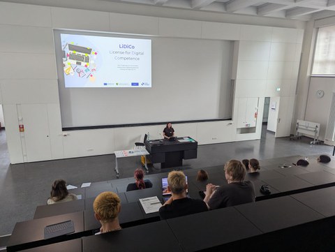 Hörsaal mit Blick auf die Präsentation und Lehrperson sowie die Rückenansicht der Teilnehmenden