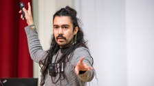 Gustavo Rosales präsentiert seinen Science Slam und zeigt in Richtung Kamera.