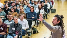 Gustavo Rosales präsentiert seinen Science Slam vor Publikum. Er deutet auf seine Präsenation