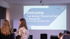 The picture shows a seminar room where a welcome slide for the event is shown.