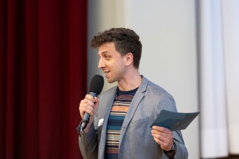 Der Moderator spricht in das Mikrofon, das er in der Hand hält.