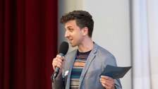 Der Moderator spricht in das Mikrofon, das er in der Hand hält.