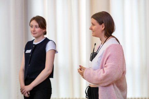 Eine Studentin hält einen Vortag. Sie steht rechts, links ist ihre Komilitonin zu sehen.