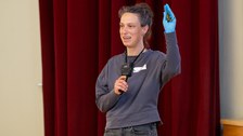 Eine Studentin hält einen Vortrag und hält mit einer Hand einen Salamander aus Plastik hoch.