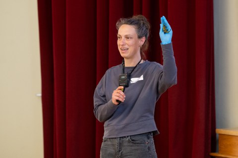 Eine Studentin hält einen Vortrag und hält mit einer Hand einen Salamander aus Plastik hoch.