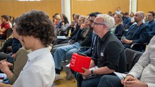 Ein Mann im Publikum hält eine rote Mikrofonbox und stellt eine Frage.