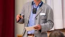 Ein Student hält einen Vortrag. Das Publikum ist unten im Bild verschwommen zu sehen.