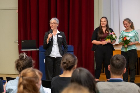 Eine Frau hält eine Dankesrede. Im Hintergrunde sind Personen mit Blumen in der Hand zu sehen.